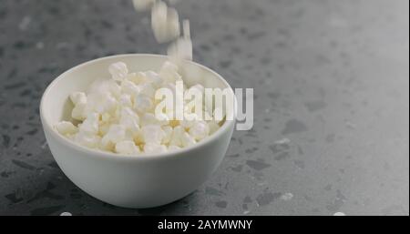 cottage cheese falling into white bowl on concrete surface, wide photo Stock Photo