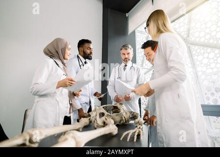 Team of young diverse doctors, students, scientists in white labcoats having discussion on the meeting in modern classroom. Young doctors colleagues Stock Photo
