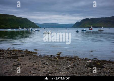 Boats that are anchored in Loch Portree off the harbor of  the village of Portree, Isle of Skye, Scotland, on a cloudy day, seen from the rocky shorel Stock Photo