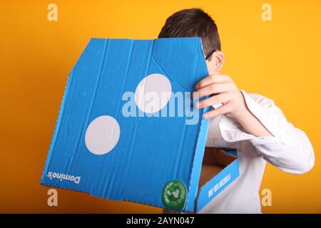 A young boy wearing glasses aged 12 years old with a large Domino's Pizza box on yellow background Stock Photo