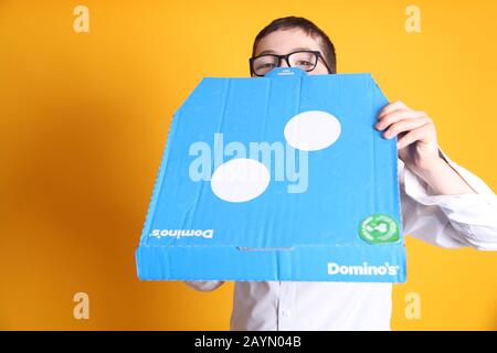 A young boy wearing glasses aged 12 years old with a large Domino's Pizza box on yellow background Stock Photo