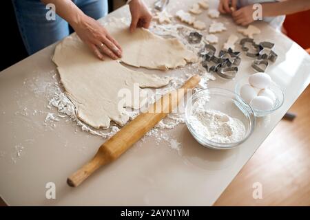 woman and her child making dough for cookies. close up cropped photo. rolling pin, eggs, two bowls are on the table Stock Photo