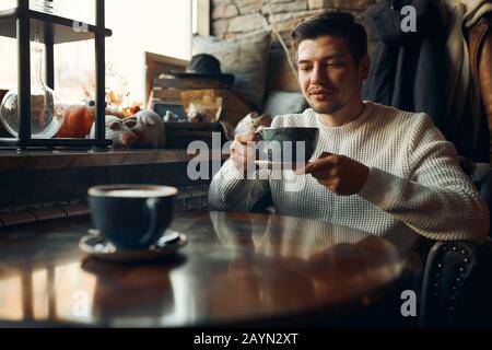 serious attractive man in stylish white sweater holding a cup of tea, enjoying peace and quite, tasty coffee for real men, relaxation Stock Photo