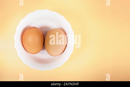 Pair of brown eggs in white bowl on pastel yellow background with copyspace. Clipping path for easy cut out for replace background Stock Photo