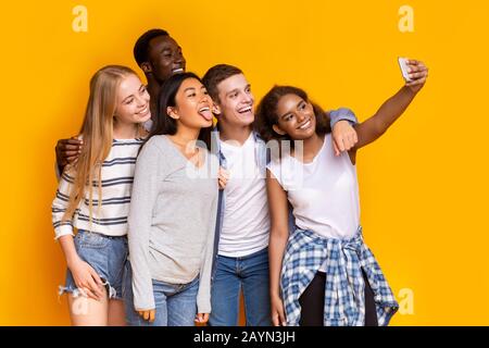 Cheerful group of multiethnic friends taking selfie over yellow background Stock Photo