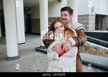 Two attractive cheerful young people hugging in the street. man standing behind her girlfriend, trying to get her warm. love, positive feeling and emo Stock Photo