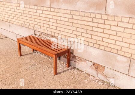 A wooden bench in front of a brick wall on a sidewalk Stock Photo