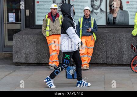 A male in designer clothing walking past some builders on a tea break having visited London Fashion Week in Strand, London, UK. Branded attire Stock Photo