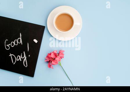 Conception good morning. Black chalk board with the inscription good day, a cup of pink coffee coffe on a light blue background. Top view. Flat lay Stock Photo