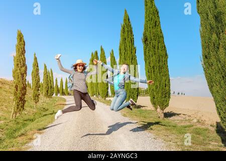 Happy friends jumping while Vacation and travel in famous cypress alley, Tuscany and Italy tourist destination Stock Photo