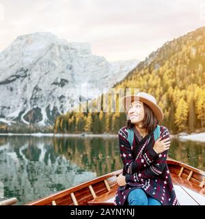 Happy asian woman sitting in wooden vintage boat floating and sailing on a Braies lake in Italian Alps mountains, Travel and dream vacation concept Stock Photo