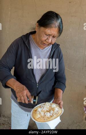 A native American woman is making Indian fry bread in front of her house at the Taos Pueblo which is the only living Native American community designa Stock Photo