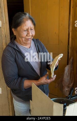 A native American woman is making Indian fry bread in front of her house at the Taos Pueblo which is the only living Native American community designa Stock Photo