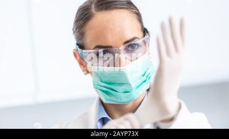 Doctor woman surgeon specialist in sterile clothing putting on surgical gloves. Stock Photo