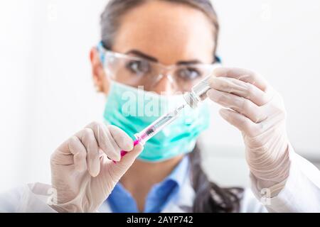 Female doctor working with syringe needle and ampoule of medicine. A scientist in sterile clothes is making a vaccine drug. Stock Photo