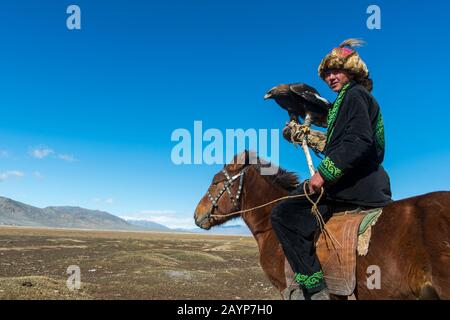 A Kazakh eagle hunter on horseback with his Golden eagle (Aquila chrysaetos) in the Sagsai Valley in the Altai Mountains near the city of Ulgii (Ölgii Stock Photo