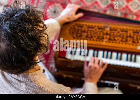 High angle view of young male shamanic playing kirtan music using musical instrument harmonium for meditation and positive vibrations Stock Photo