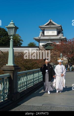 A wedding couple in traditional clothing is posing in front of the castle at the Kanazawa Castle Park in Kanazawa, Ishikawa Prefecture, on Honshu Isla Stock Photo