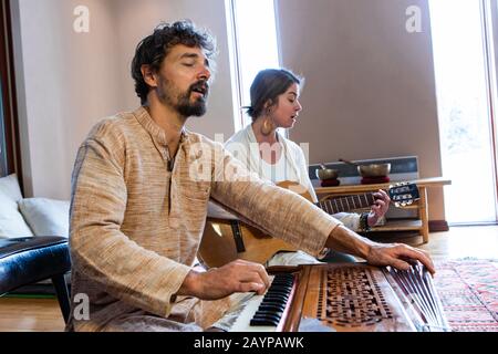 Senior man with woman playing musical instrument harmonium and classical guitar together as sacred and kirtan music for meditation and peace Stock Photo