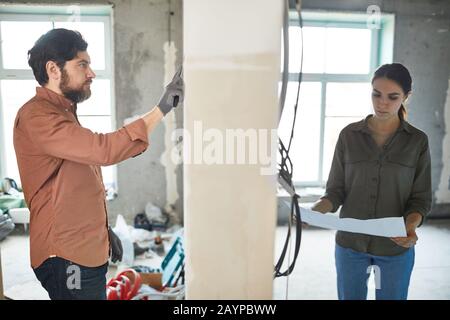 Portrait of married couple doing home renovations, man and woman separated by wall in house under construction, copy space Stock Photo