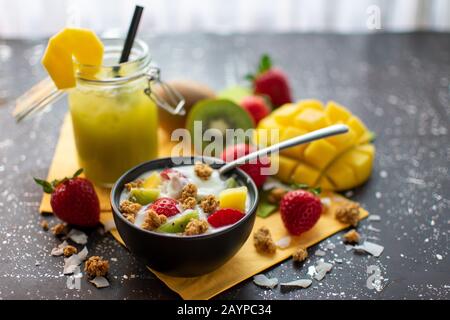 healthy breakfast: crispy muesli with yoghurt fresh strawberries, kiwis, mangoes, coconut flakes and spoon Stock Photo