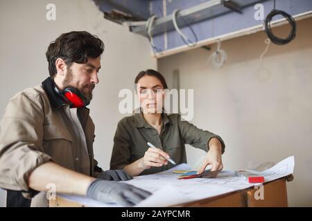 Portrait of young woman looking at floor plans with building contractor while while discussing home renovations, copy space Stock Photo