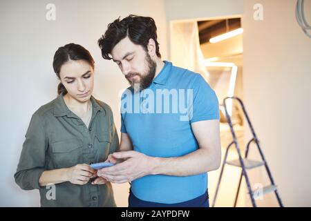 Waist up portrait of married couple using smartphone for design ideas while renovating house together, copy space Stock Photo