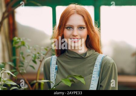 Young red hair woman farmer portrait looking camera and smile in greenhouse. Spring home gardening concept. Stock Photo