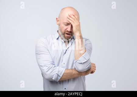 Mature caucasian man having headache feeling tired after hard day. Studio shot. Negative facial human emotion. Stock Photo