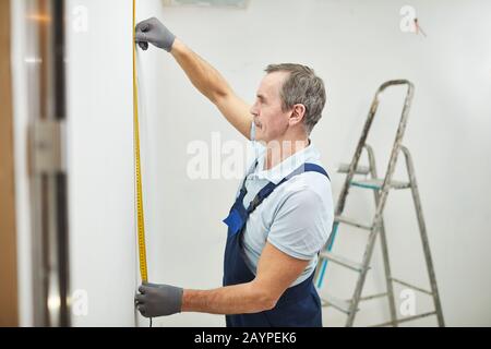 Side view portrait of senior construction worker measuring wall while renovating house, copy space Stock Photo