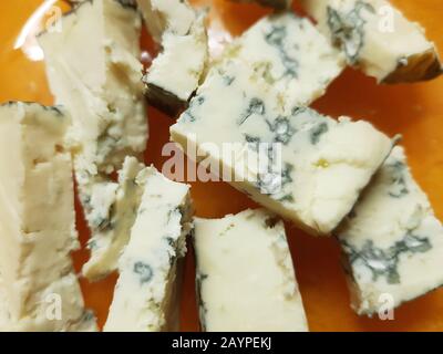 Pieces of dorblu cheese on an orange plate, close-up. Stock Photo