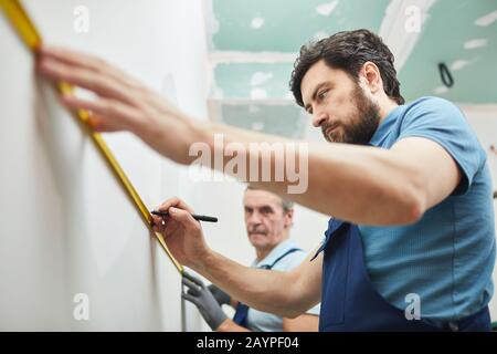 Low angle portrait of two construction workers measuring wall while renovating house, copy space Stock Photo