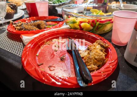 Red plastic disposable plate on a table after eating buffet food at a party Stock Photo