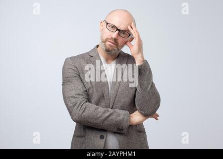 Thinking man in glasses scratching his head being confused. Close up portrait of a casual mature pensive businessman. Studio shot Stock Photo