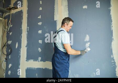 Portrait of senior man working on dry wall while renovating house, copy space Stock Photo