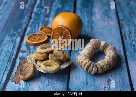 Sun-dried figs on a small plate. A dried fig wreath besprinkled with powdered sugar. A grapefruit and dried orange slices are in a blurry background. Stock Photo