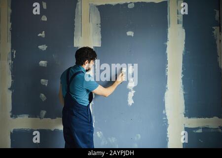 Back view portrait of bearded man working on dry wall while renovating house, copy space Stock Photo