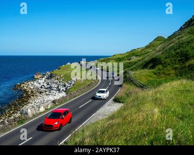 The eastern coast of Northern Ireland and Antrim Coast Road A2, a.k.a Causeway Coastal Route with cars. One of the most scenic coastal roads in Europe