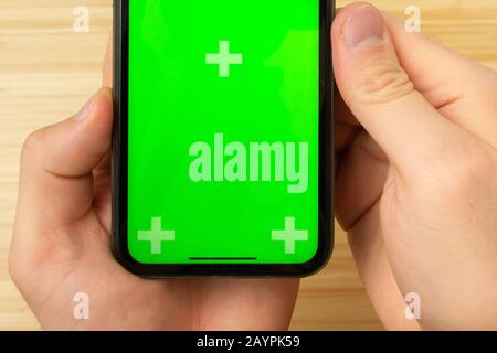 Mockup image of hand holding black mobile phone with green screen in the office table on the background Stock Photo