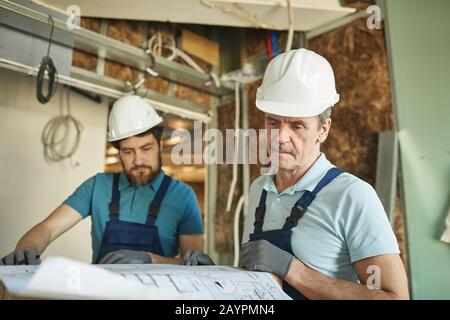 Portrait of senior construction worker wearing hardhat while looking at floor plans while renovating house, copy space Stock Photo