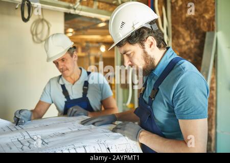 Side view portrait of bearded construction worker wearing hardhat while looking at floor plans while renovating house, copy space Stock Photo