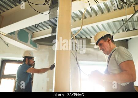 Side view at two construction crew workers separated by wall while renovating house, copy space Stock Photo