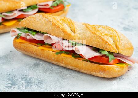 Two Long baguette Sandwiches with arugula, slices of fresh tomatoes, ham and cheese Stock Photo