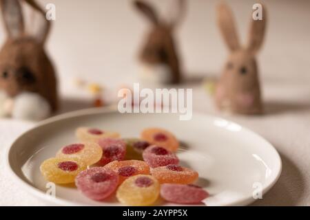Three brown felt bunnies waiting for jellybeans candies in a white plate in foreground. Bunnies out of focus, close-up, high angle view. Stock Photo