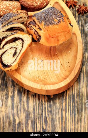 Fresh slices of roll with poppy seeds on a wooden surface, next to cookies, anise stars in blur, close-up, copy space, vertical image. Stock Photo