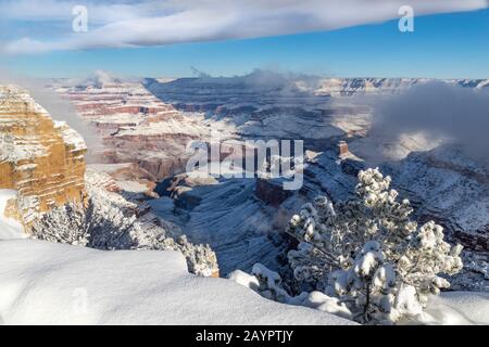 Grand Canyon in winter, viewed from the South Rim. Snow covers the canyon walls. Clouds clinging to the canyon, and overhead in the blue sky. Edge of Stock Photo