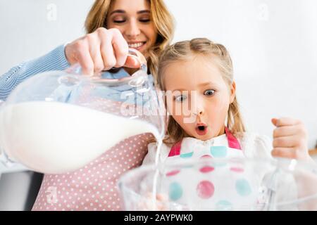 Low angle view of shocked daughter looking at mother pouring milk from jug in bowl Stock Photo