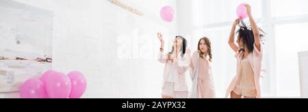 panoramic shot of cheerful multicultural girls having fun with pink balloons on bachelorette party Stock Photo