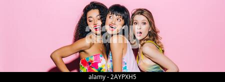 panoramic shot of beautiful fashionable multicultural girlfriends posing on pink Stock Photo