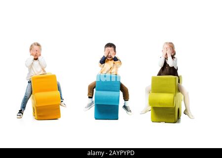 multicultural children closing eyes and sitting on puzzle chairs, isolated on white Stock Photo
